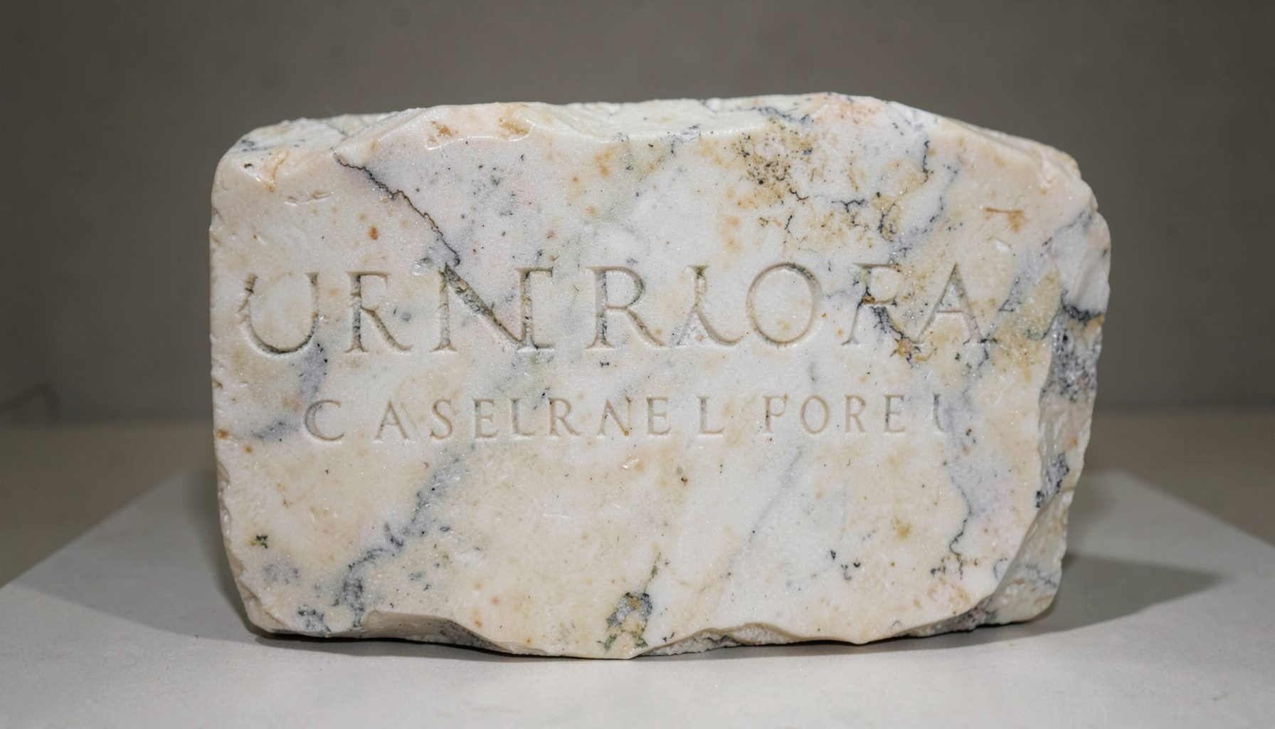 A weathered marble inscription fragment in soft cream and pale gray, shallow carved lettering catching side light, quiet and timeless mood