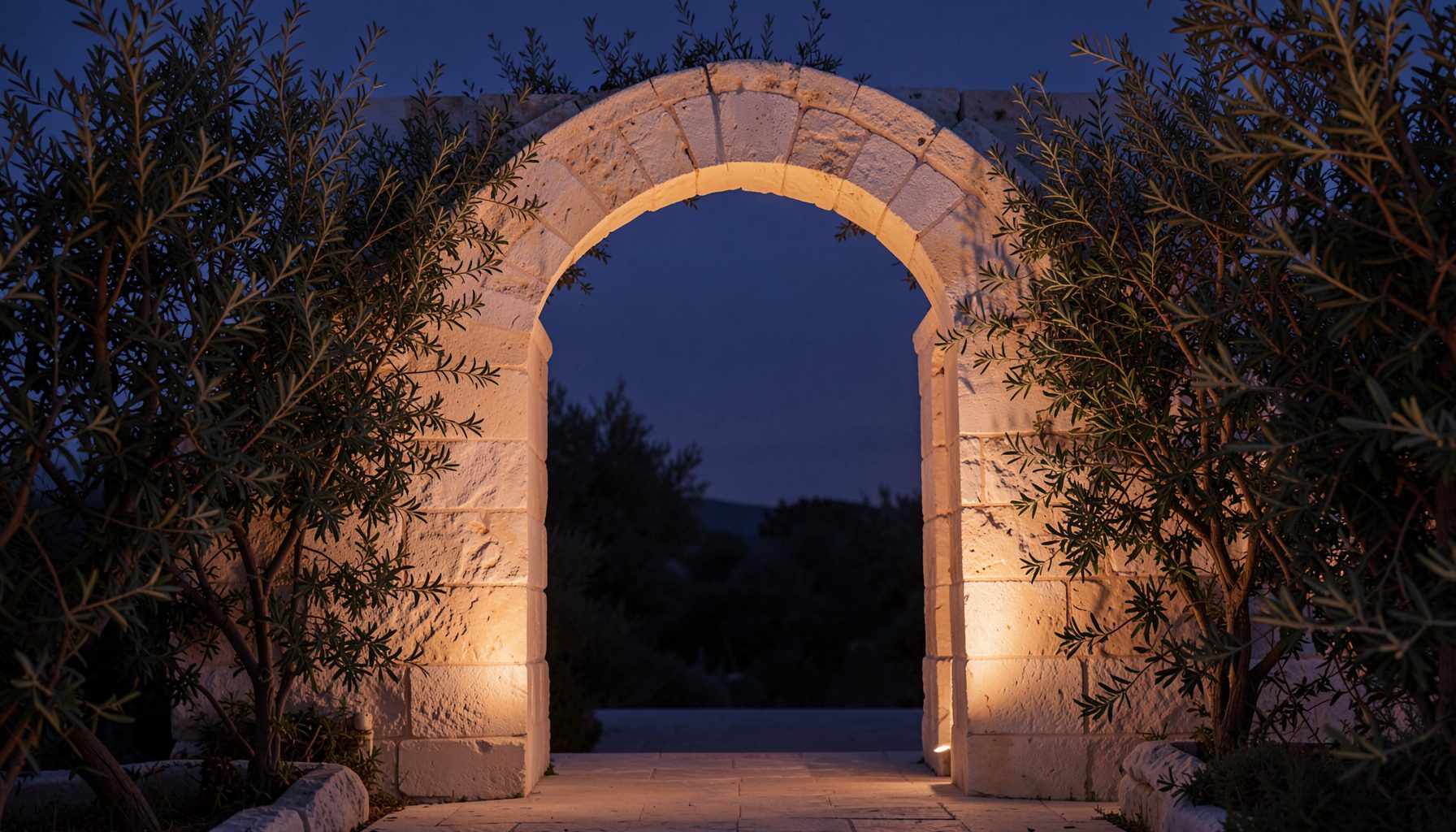 A softly lit stone archway framed by olive branches against a dusky indigo sky, warm ivory stone tones